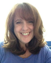 Sheila J. Gibbons smiling with long light brown wavy hair wearing a blue crew neck top