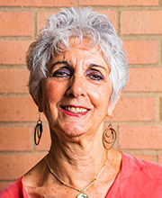 headshot photo of Roberta Guez with short wavy gray hair wearing a salmon top and long earrings