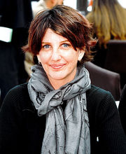 Kristy Hill smiling with medium length brown hair wearing a black long sleeve top and a gray fashion scarf with print of the Eiffel Tower