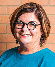 headshot photo of Professor Kathleen McAleer with short light brown hair wearing glasses and a blue top