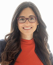 headshot photo of Dr. Michele Meek with long dark brown hair wearing brown rim glasses, a red top and black zipper up jacket