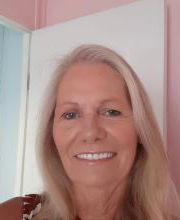 Nancy Monroe smiling with long gray/blonde hair in front of a white door on a pink wall