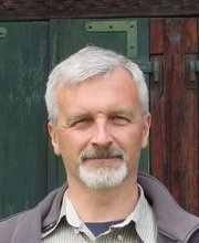 headshot photo of Dr. Kenneth Paulsen with short grey hair, mustache and beard wearing dark blue shirt under white and light grey checkered button up shirt under a grey zipper up fleece jacket