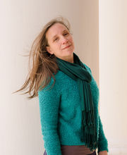 Jennifer Schoonover smiling standing next to a large white column on the portico of Boyden Hall with long straight light brown hair wearing a teal blue sweater and green scarf