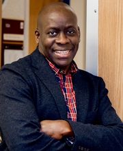 Dr. Jibril Solomon smiling with his arms folded and wearing a navy blazer over a navy and red button down shirt