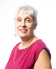 headshot of Elizabeth Souffront smiling with short gray hair wearing a sleeveless fuschia pink blouse and long earrings