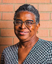 headshot of Josephine St. Cyr Saieh with short curly black and gray hair wearing glasses and a v-neck houndstooth pattern black and white top