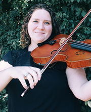 Dr. Cassie Sulbaran smiling with medium length brown wavy hair wearing a black short sleeve top and playing a violin