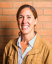 headshot of Dr. Pam Szczygiel with long brown hair pulled back in a low pony tail wearing a white and blue blouse under a tan jacket