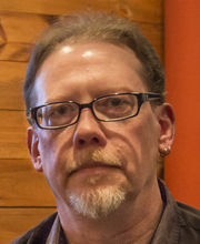 headshot photo of Tony Schultz with receding light brown hair and graying beard and mustache wearing thin black rim glasses and a brown button down shirt
