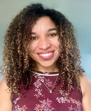 Dr. Maggie Veiga smiling with medium long curly dark brown hair with highlights and wearing a sleeveless maroon top with white and pink leaves on it