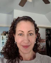 Dr. Michele Wakin smiling with long curly brown hair pulled back with a headband and wearing a gray sweater