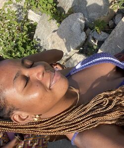 a smiling woman wearing gold jewelry and braids