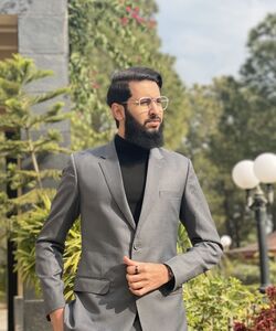 a dark haired man wearing glasses and a grey jacket