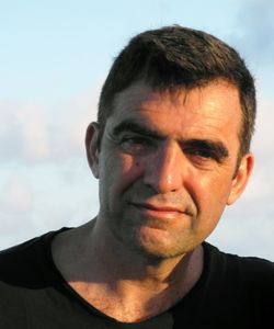 a dark haired man in a black shirt against a light blue background
