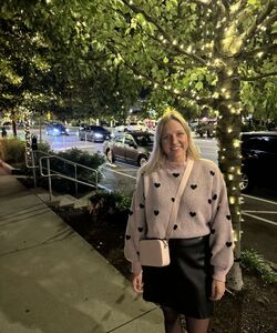 A smiling blonde woman standing on a sidewalk under a tree