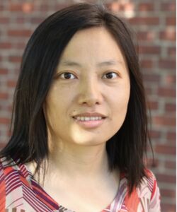 Hui Zhang smiling with medium length dark brown hair and wearing a red and gray top