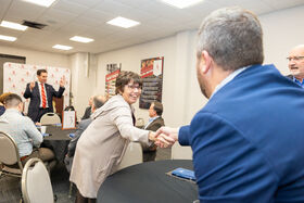 A woman reaches across a table to shake a man's hand