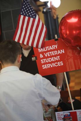 A student talks with a BSU representative at a table decorated with a Military and Veteran Student Services sign, a red balloon, and an American flag