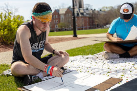 Two students sitting on the grass, practicing drawing on a sunny day