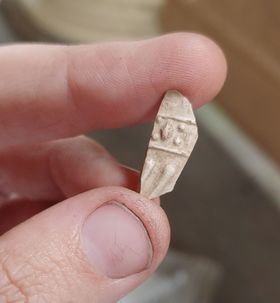 Two fingers hold a small piece of clay with symbols on it