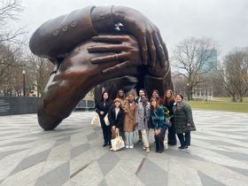 A group stands in front of a statue of two hands interlocked
