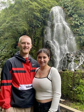 Two students stand in front of a waterfall.