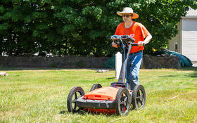 A professor pushes a ground-penetrating radar unit across a cemetery.