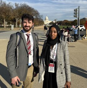 Two people pose for a photo with the U.S. Capitol in the background