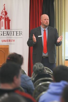 Justin McCauley, wearing a suit and a red tie, speaking to a group of families at BSU