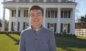 A man wearing a gray sweatshirts stands smiling