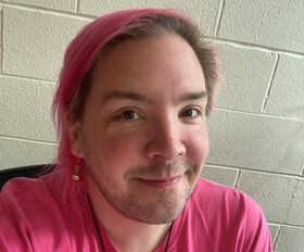 Sean Connell smiling with medium length straight brown hair with pink highlights and wearing a pink t-shirt