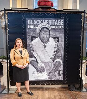 Emily Field stands next to a picture of the Phillis Wheatley stamp.