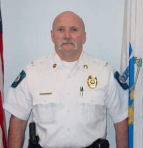 Lt. Wise stands in front of two flags while wearing a police uniform.