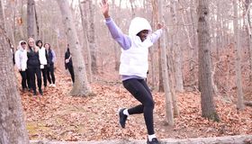 Woman wearing white jacket jumps over a log