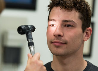 A student has a light pointed at his eye during a health checkup
