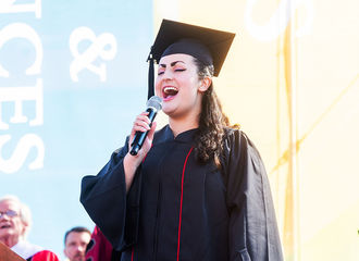 A student in a graduation cap and gown sings at the commencement ceremony