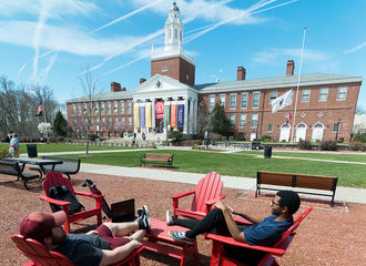 Two students relax in Adirondack chairs on the Boyden Quad, with Boyden Hall in the background