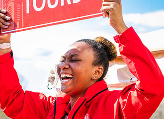 A student tour guide smiling and holding a Campus Tours sign above her head