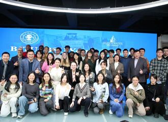 Chinese and American students pose for a group photo in front of a large digital screen.