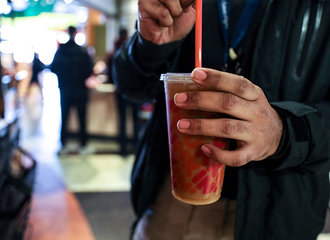 A hand holds a cup Dunkin iced coffee while the other adjusts the straw