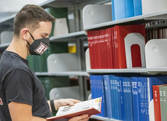 A student wearing his face mask while browsing in the library