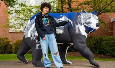 Anaisha stands next to a blue bear statue and points at it smiling
