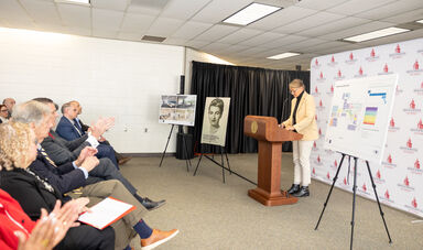 A woman stands talking at a podium while people sit an clap