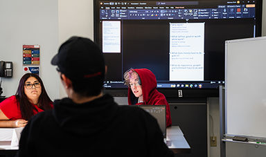 Three students work collaboratively using a large monitor.