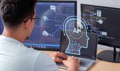 A man sits in front of a computer screen that says AI