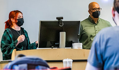 Carrie Provost stands next to a computer giving a presentation to students.
