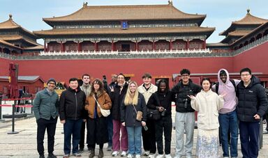 A large group of students stands next to a building in the Forbidden City.