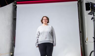 Mackenzie Cobb stands in front of a white backdrop illuminated by lights.
