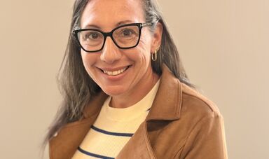 A woman wearing a striped shirt, blazer and glasses smiles